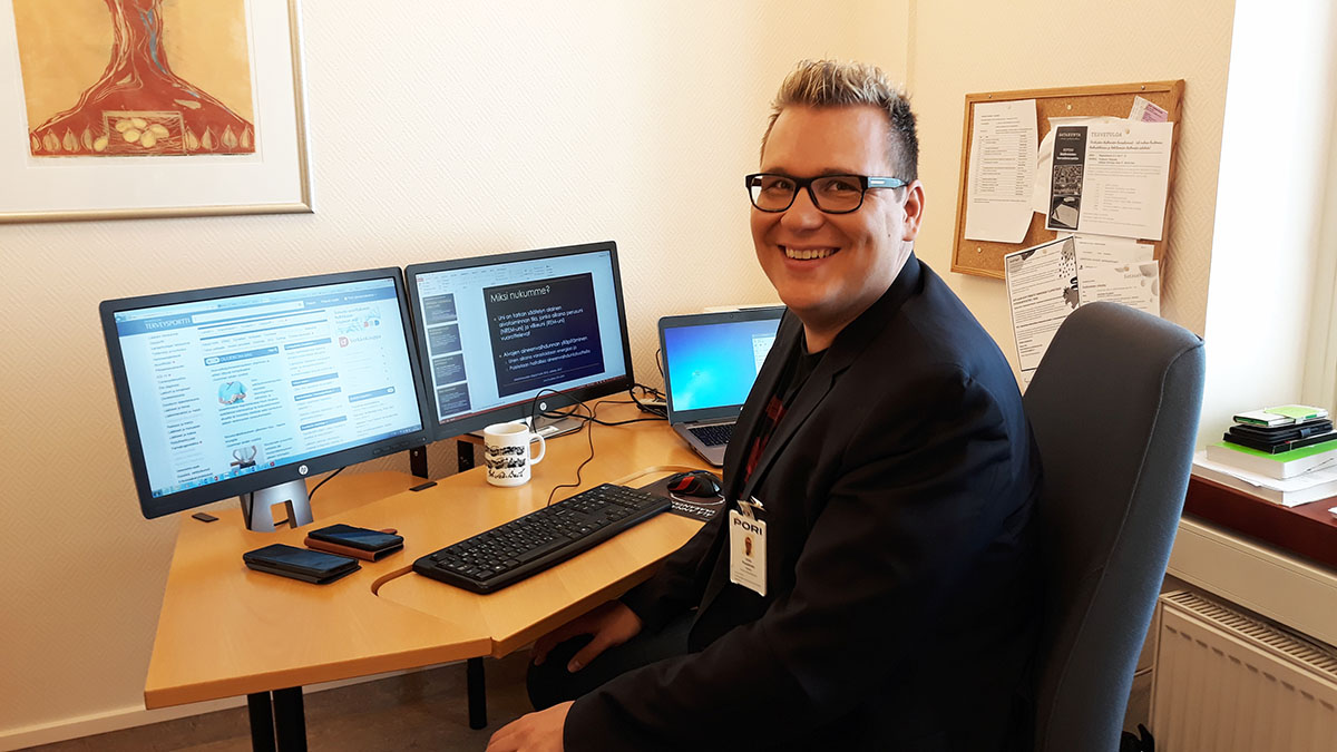 Juha Puustinen istuu työpöydän ääressä ja katsoo kameraa.