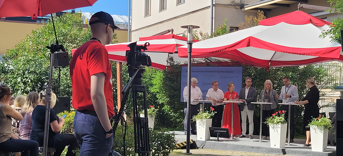 SuomiAreena-keskustelun panelistit ja etualalla videokuvaaja.