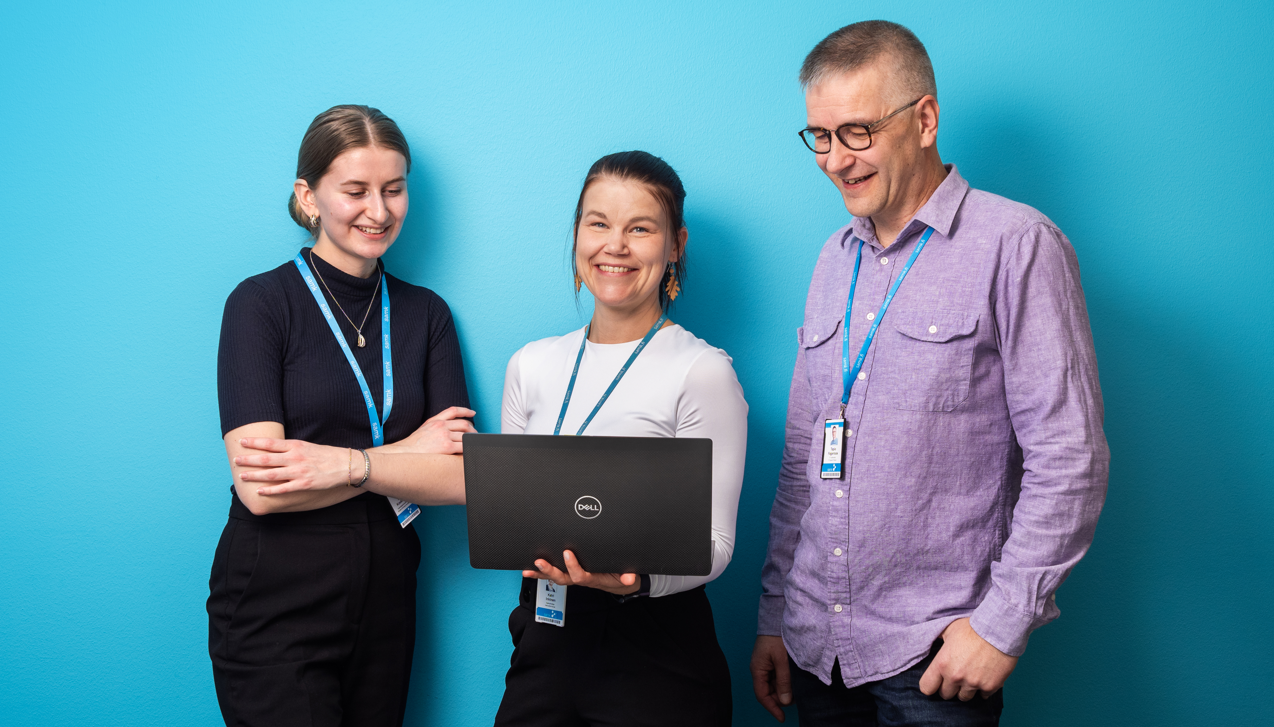 Three people are standing next to the blue wall.