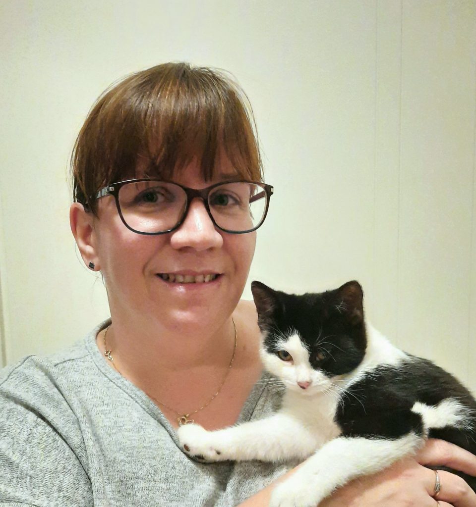 Aila Rantanen poseeraa lähikuvassa mustavalkoisen kissan kanssa.