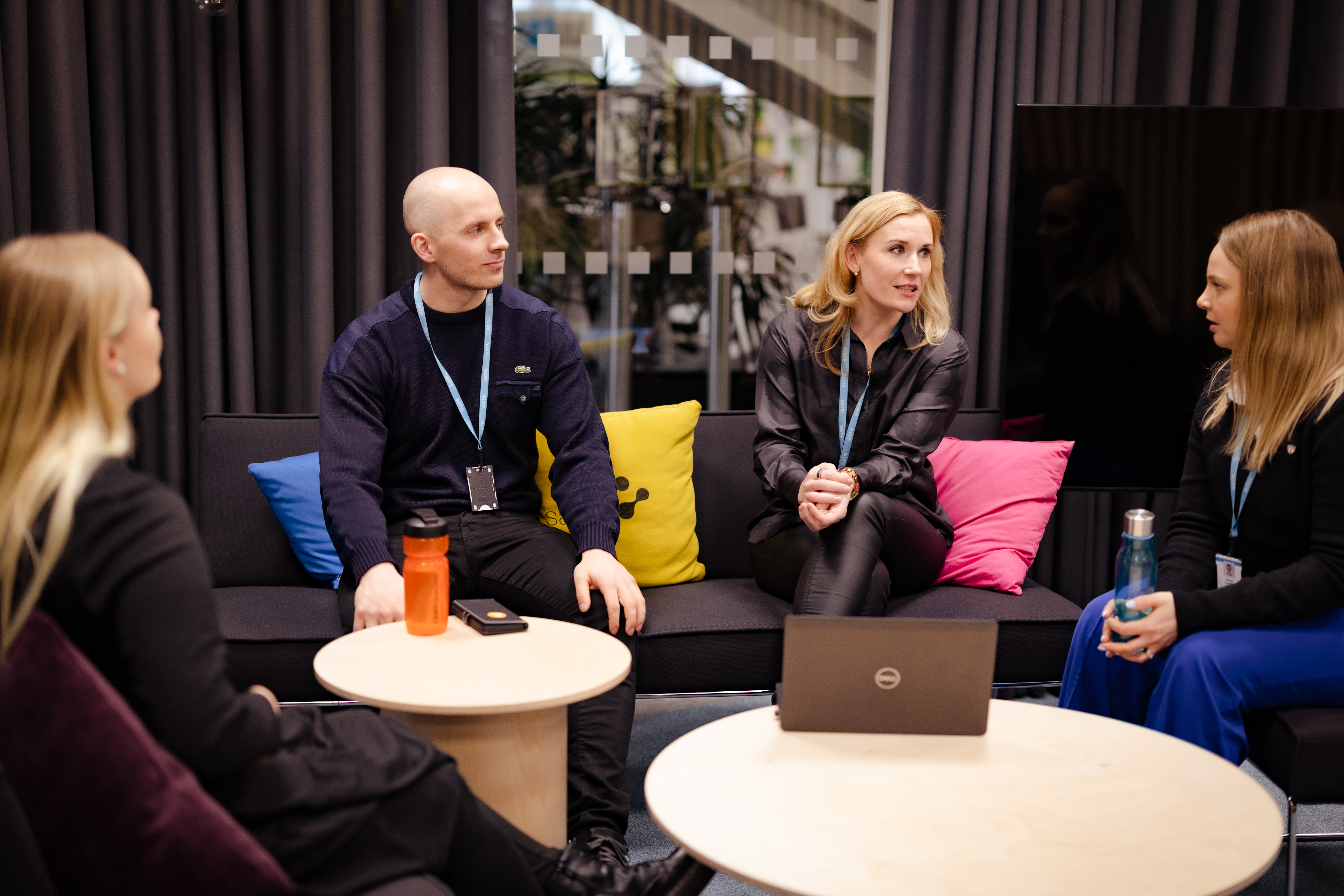 Four people sitting on sofas around tables in the middle.