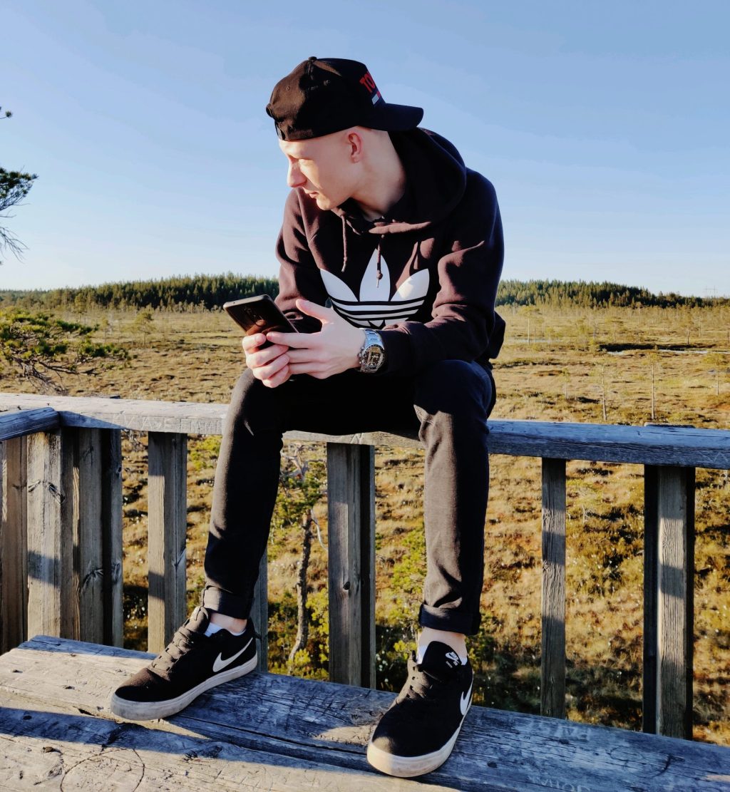 Joonas istumassa puhelin kädessä kaiteella luonnossa.