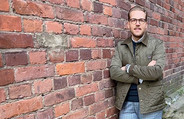 Jussi Ahlgren poseeraa kameralle ja nojaa tiiliseinään.