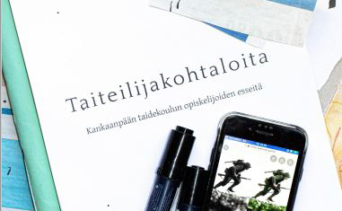 Taiteilijakohtaloita-kirja, kännykkä ja kyniä.