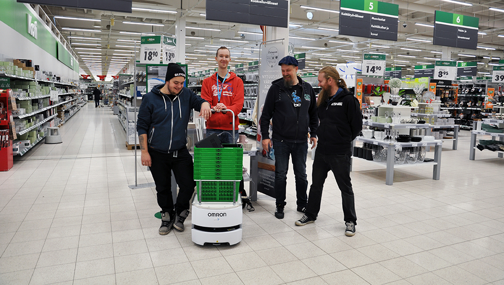 Opiskelijat poseeraavat koripalvelurobotin kanssa Prisman käytävällä.