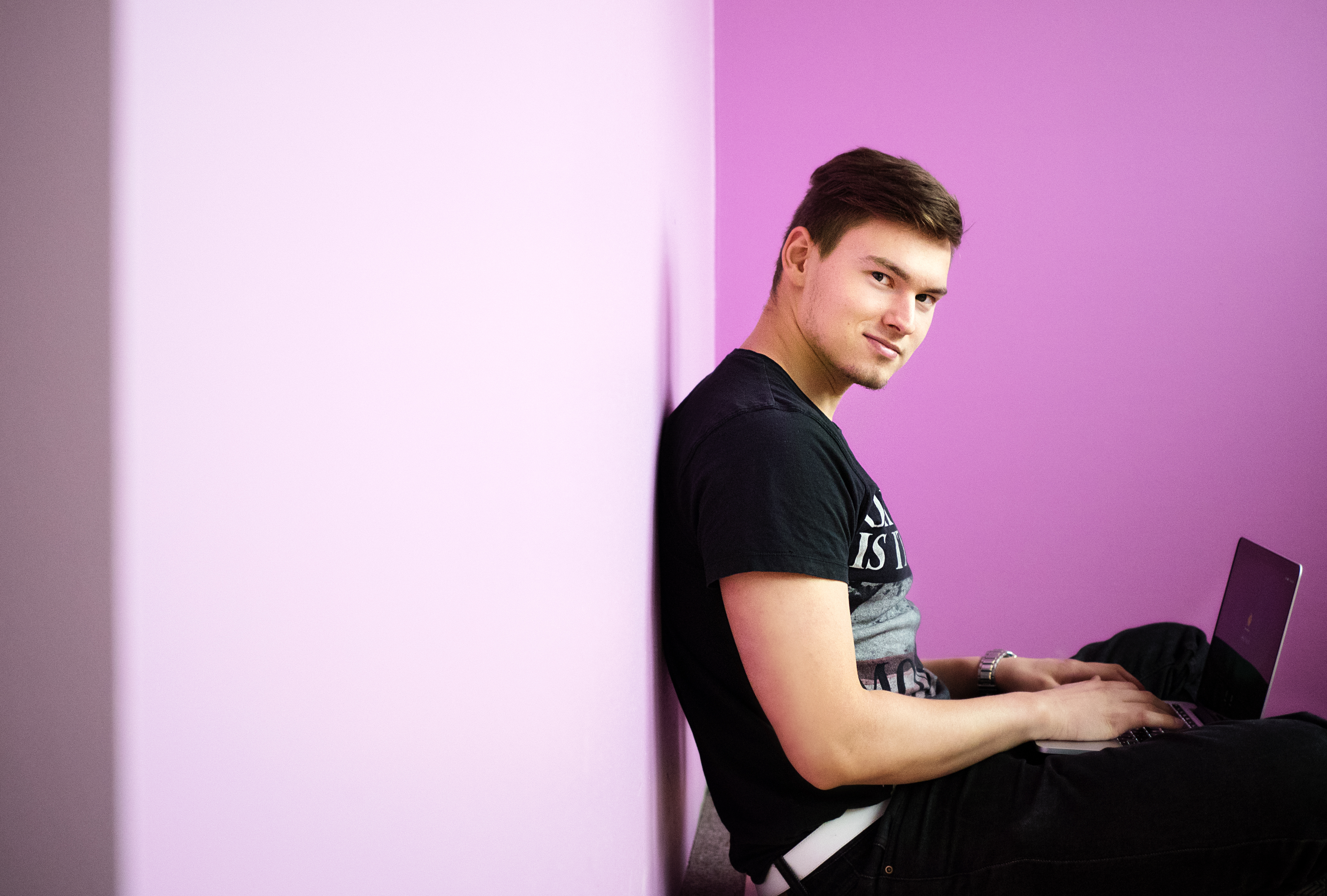Student sitting on a floor with a laptop looking at camera smiling