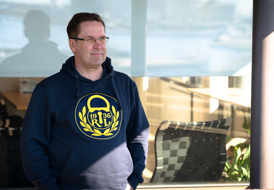 A man in a blue shirt stands on the terrace next to the window and looks ahead.