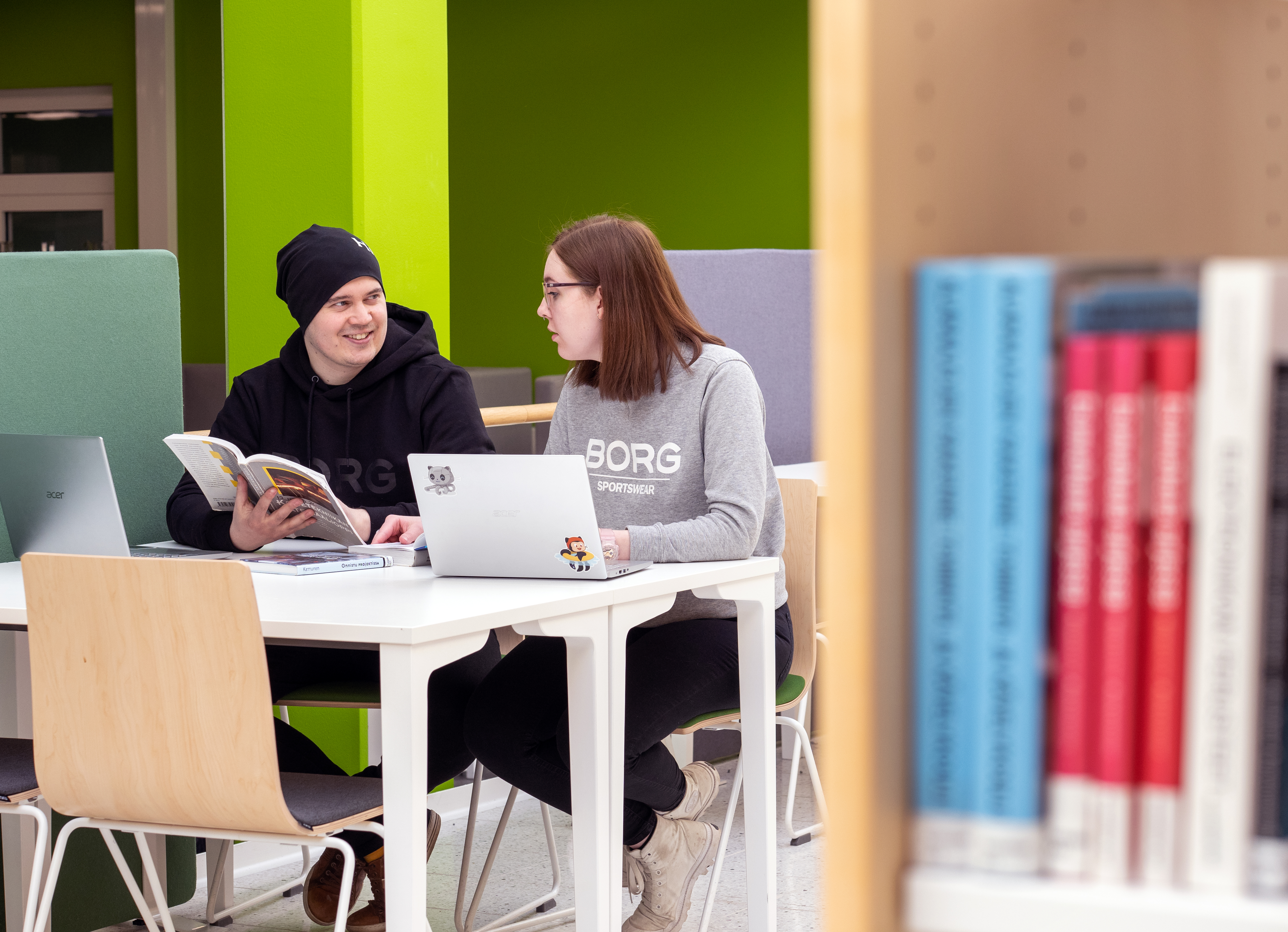 Two students chatting at a desk in the library.