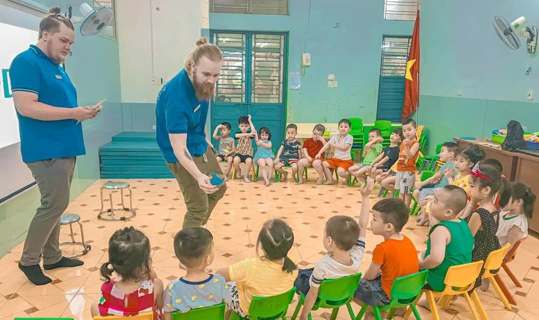 Ilkka Toivonen and Arttu Metsämäki in a teaching situation. Children sit on chairs in an arch.
