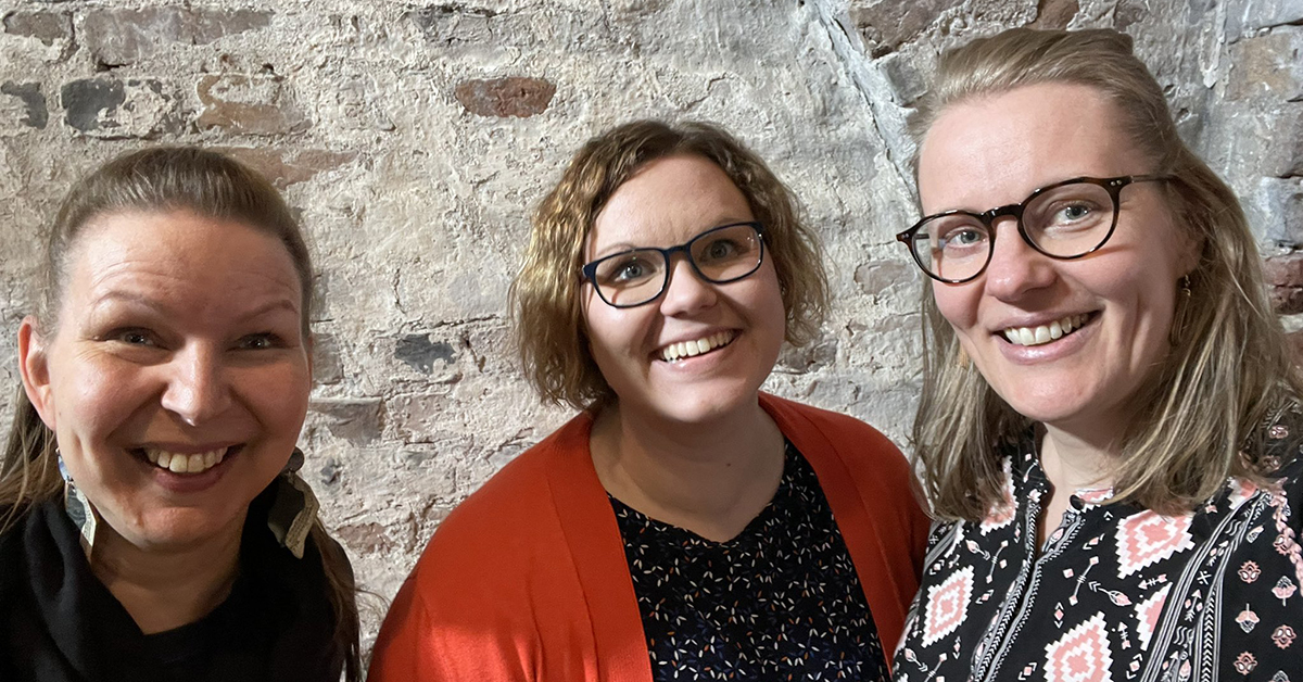 Three smiling women standing in front of a wall.