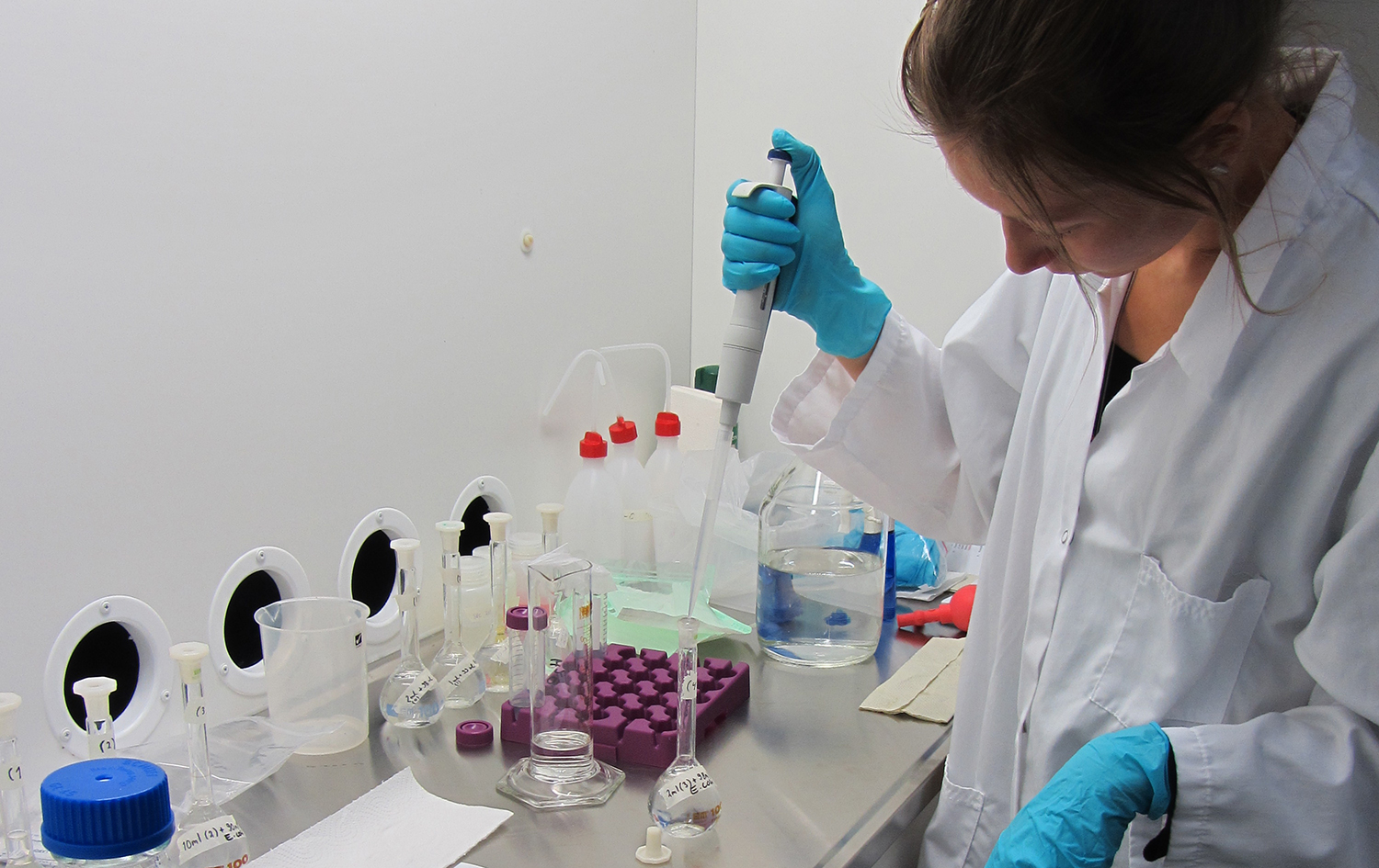 Nainen työskentelee laboratoriossa valkoinen takki päällään.
