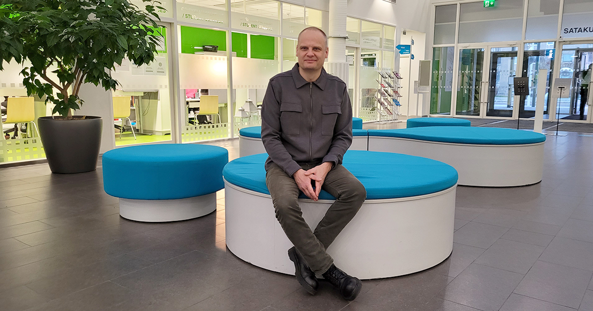 Mika Valtonen istuu SAMKin Porin kampuksen ala-aulassa turkoosilla penkillä.