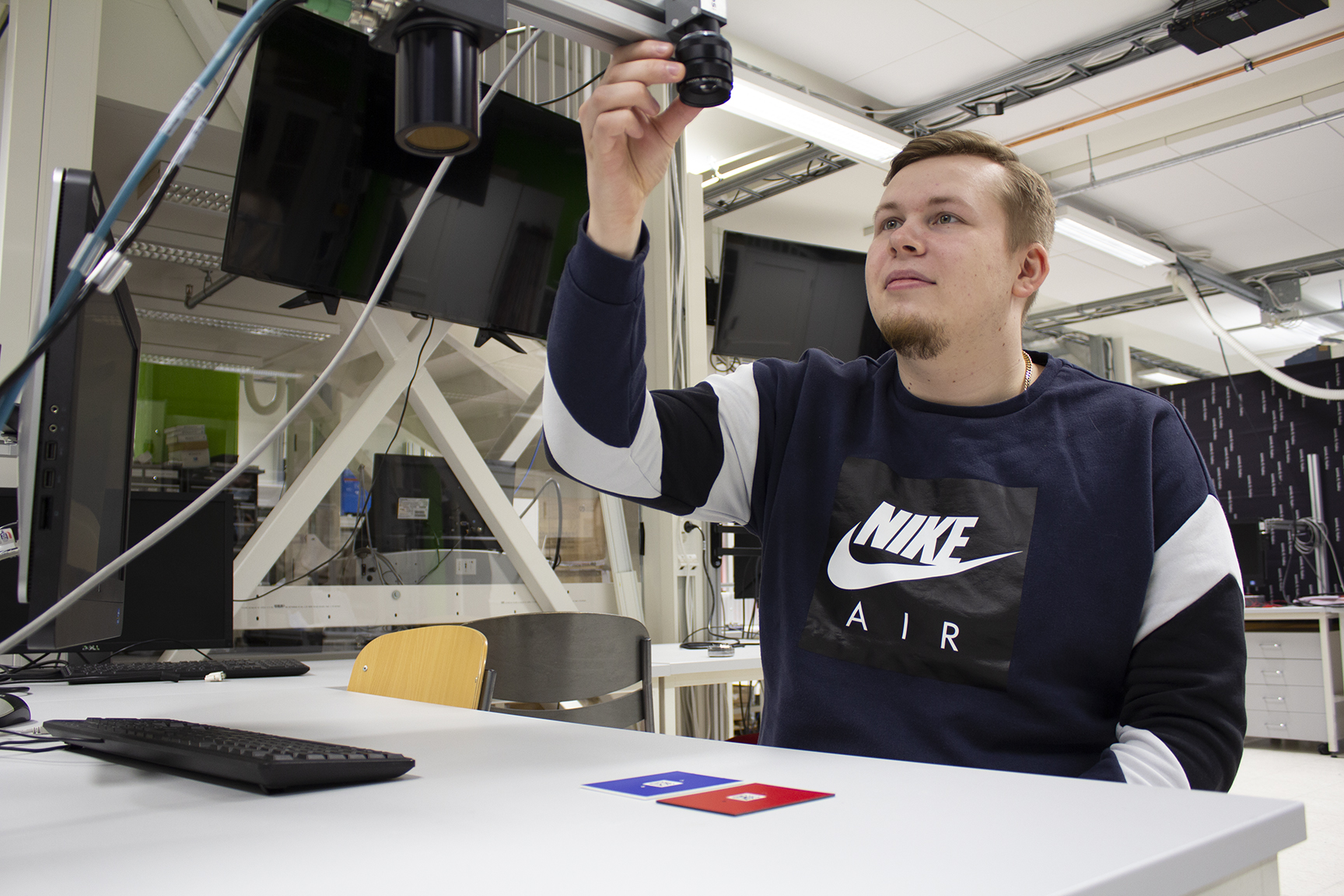 Nuori mies istuu pöydän takana ja kokeilee käsin pöydän yllä olevaa konenäkökameraa.