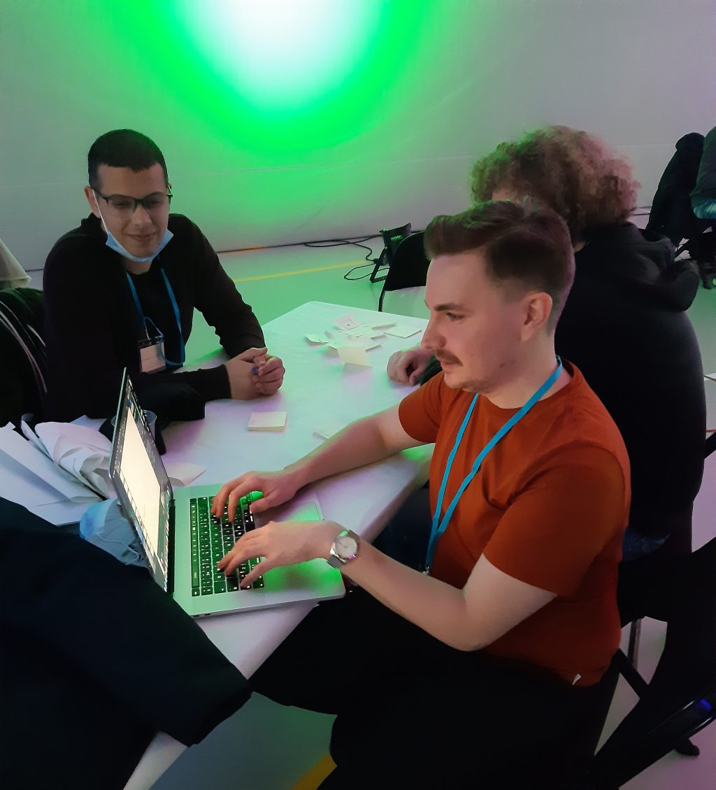 Three men sitting in front of a laptop.