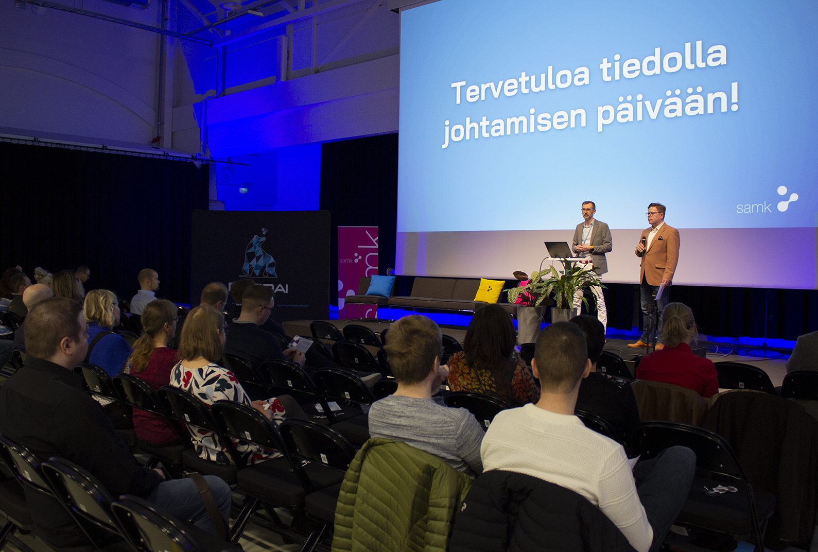 Kaksi ihmistä lavalla yleisön edessä.