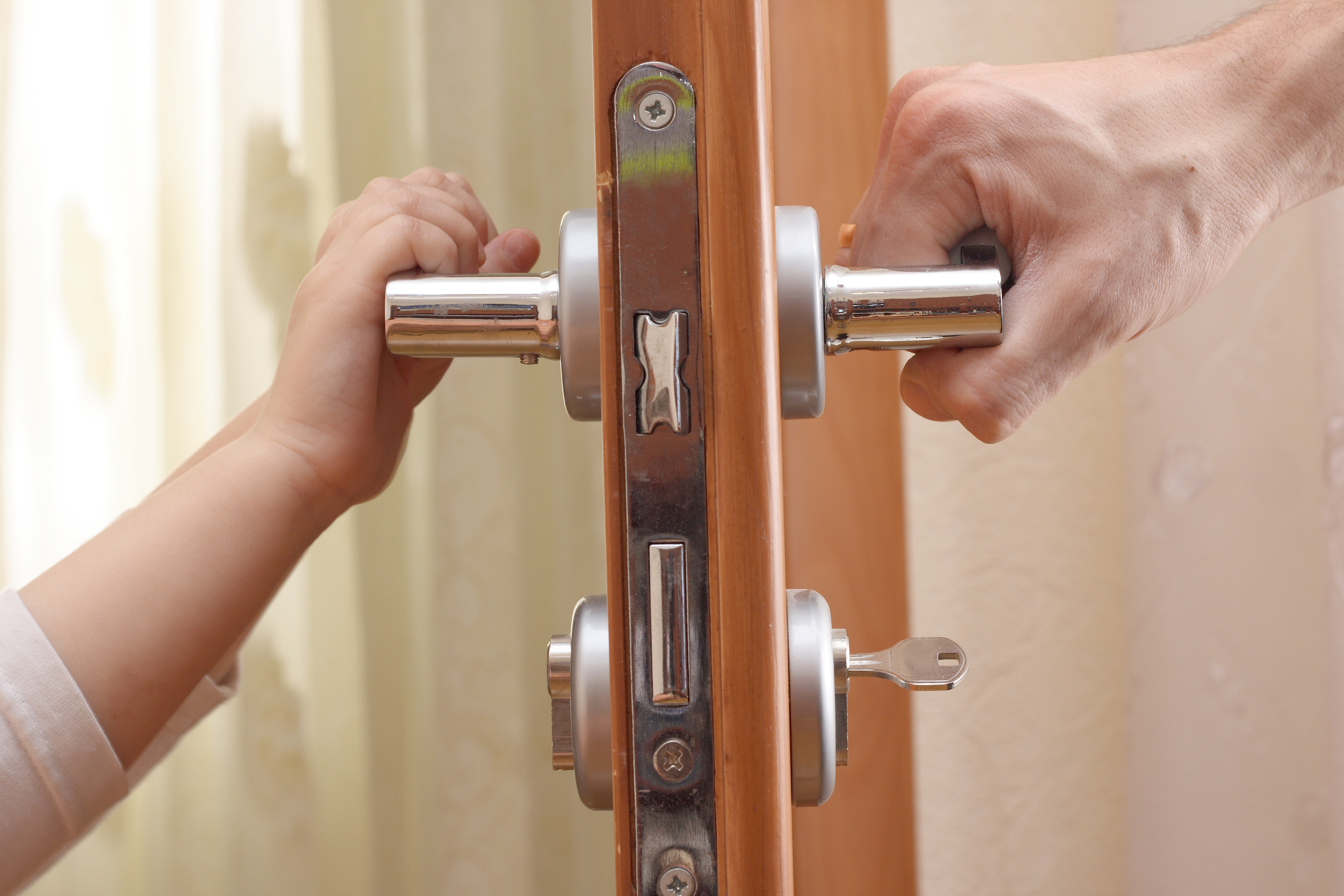 A door handle that is pressed by the hands of a child and an adult.