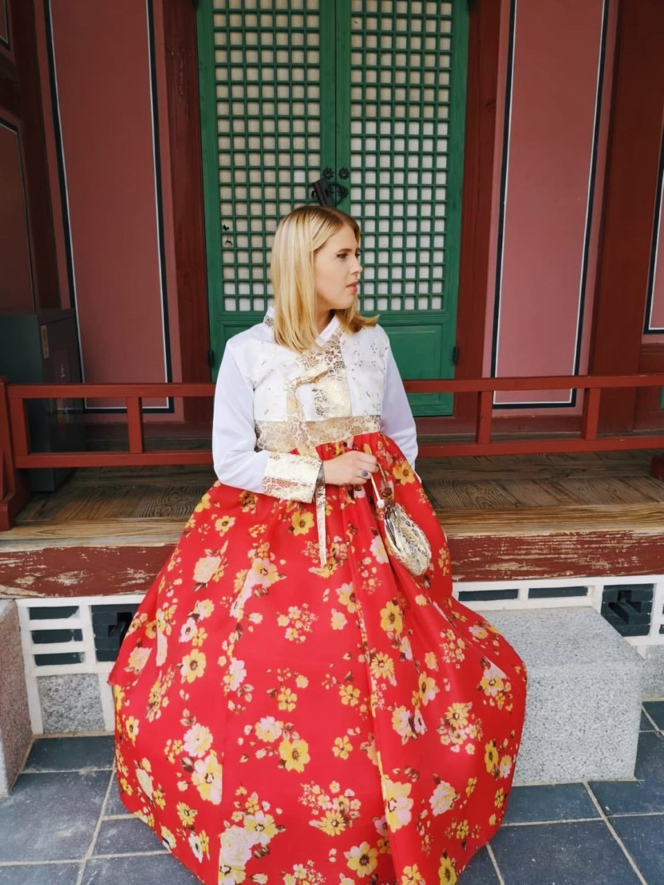 Peppi Wallinkoski istuu rakennuksen edessä, hän on vierailemassa Gyeongbokgungin palatsissa päällään korealainen kansallispuku, Hanbok.