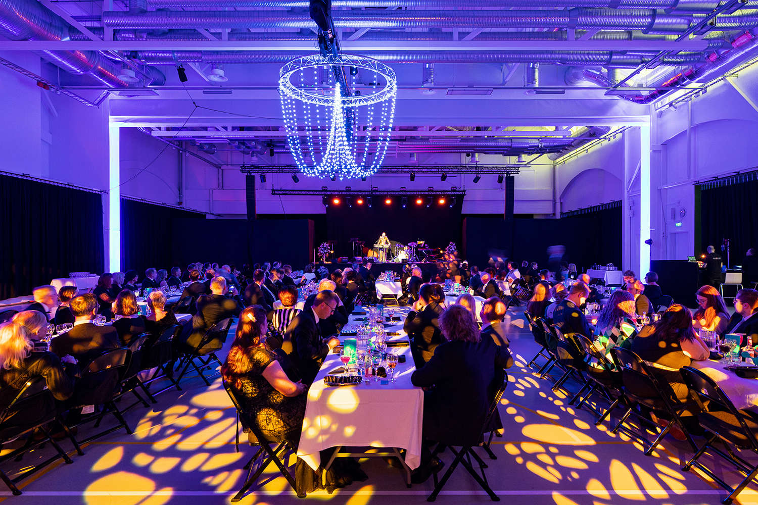 People sit at tables in a festively lit hall.