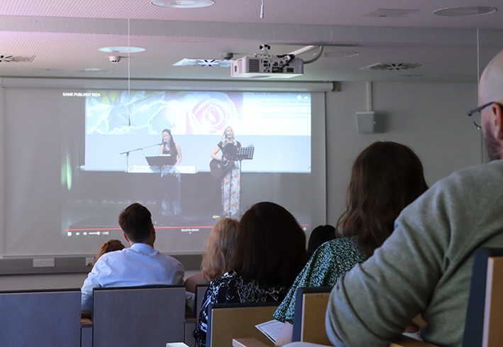 The audience listens to a musical performance on the screen.
