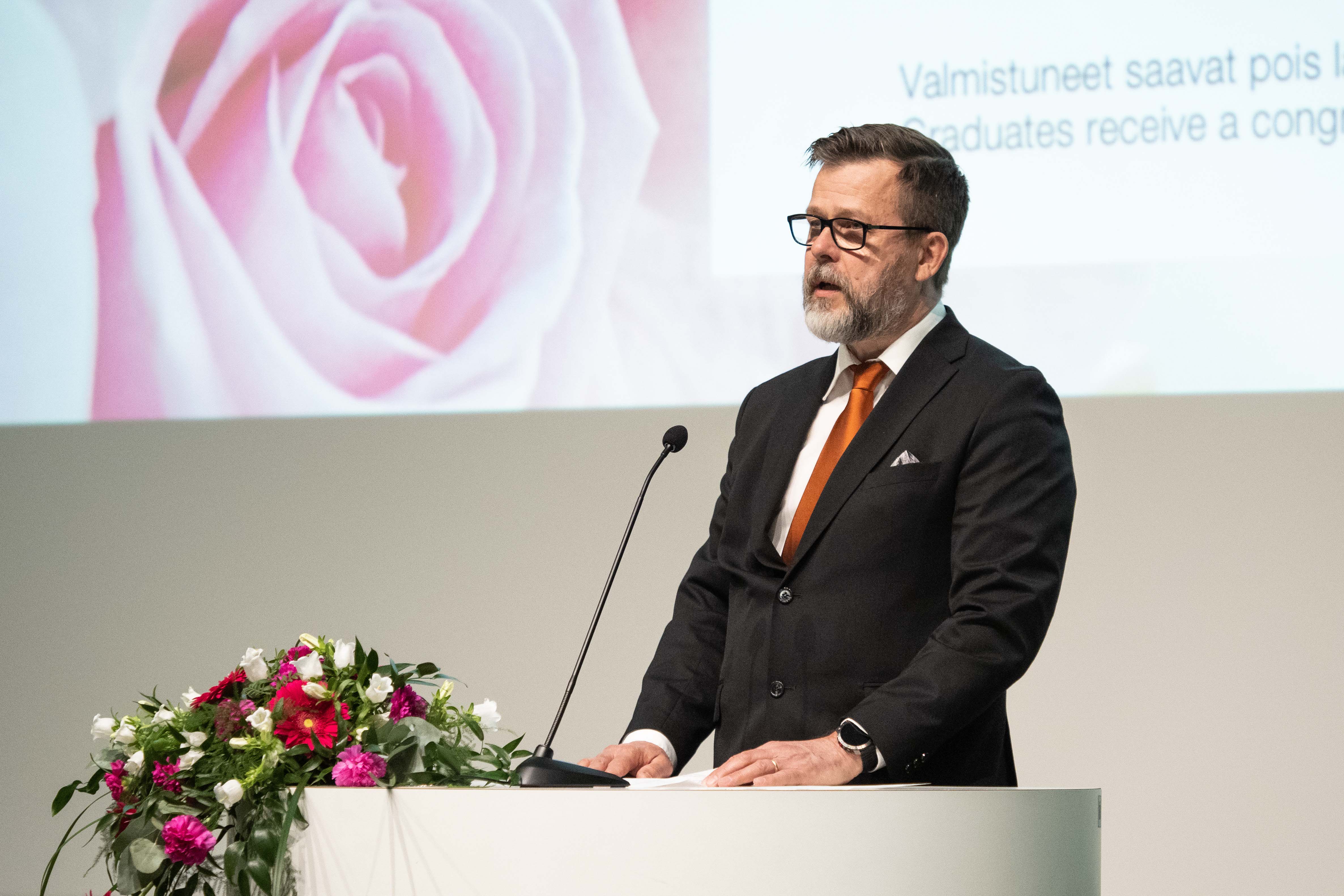 A male person speaks to the audience from a lectern.