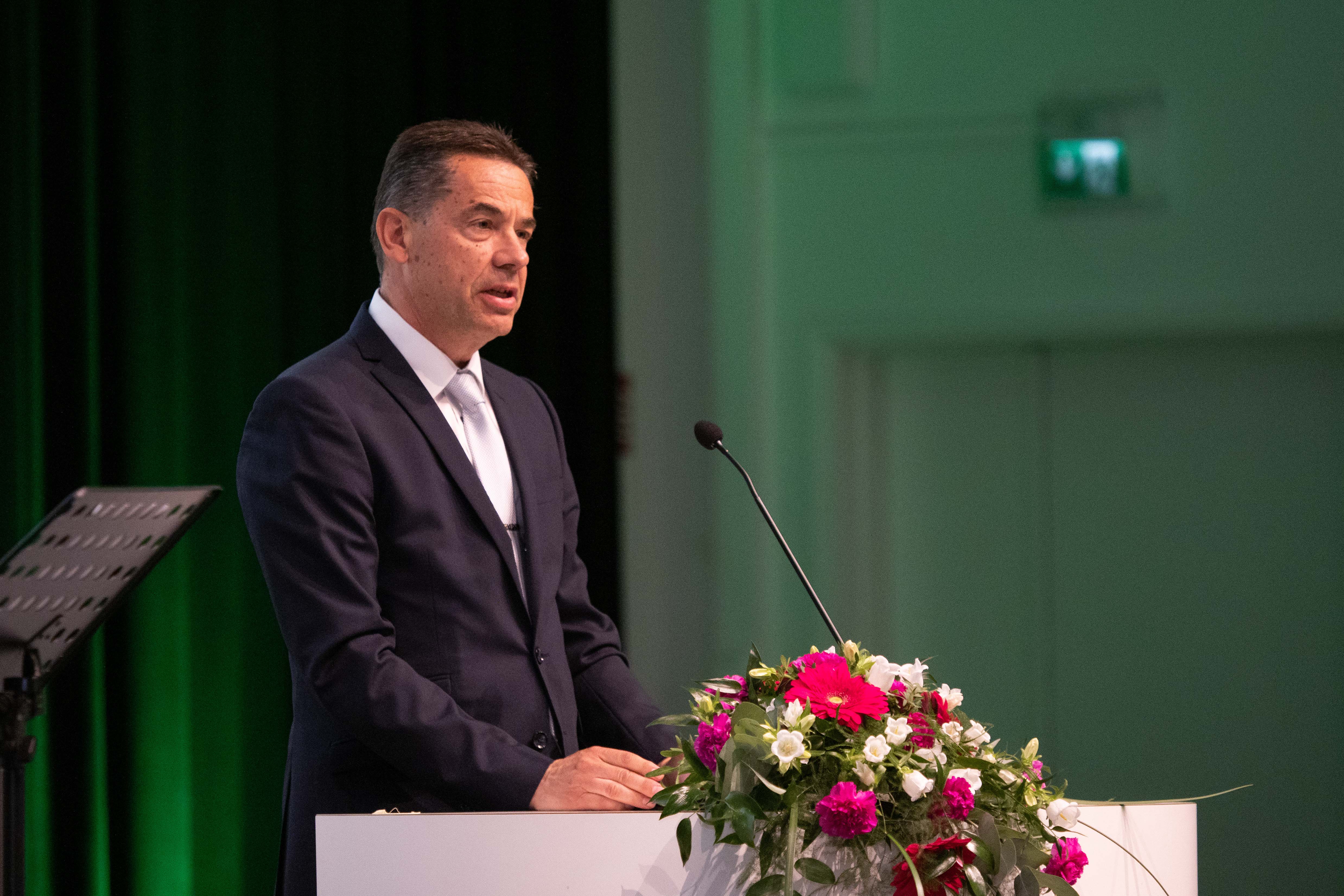 A male person speaks to the audience from a lectern.