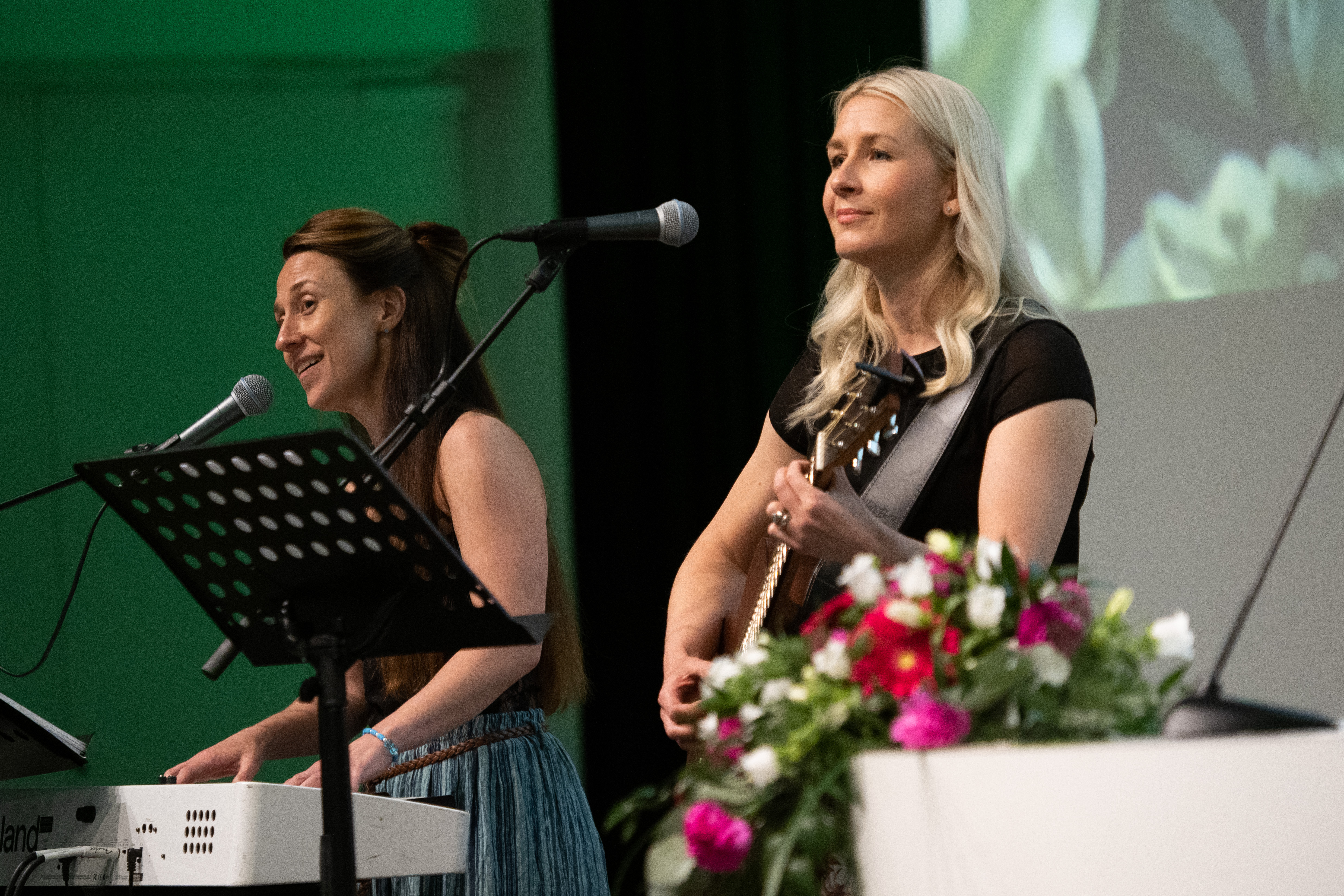 Two Two women perform on stage with guitar and keyboards.