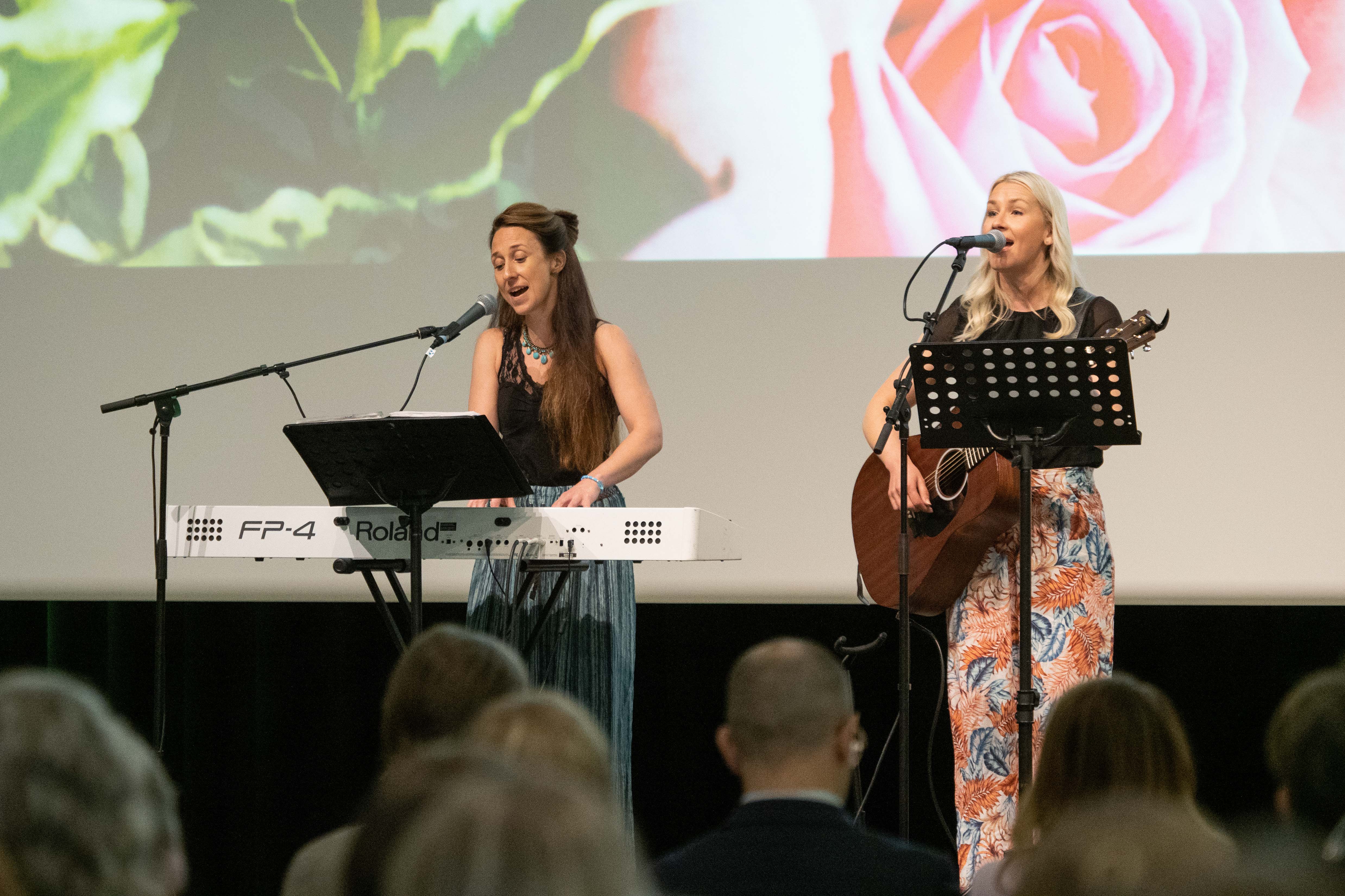 Two women perform on stage with guitar and keyboards.