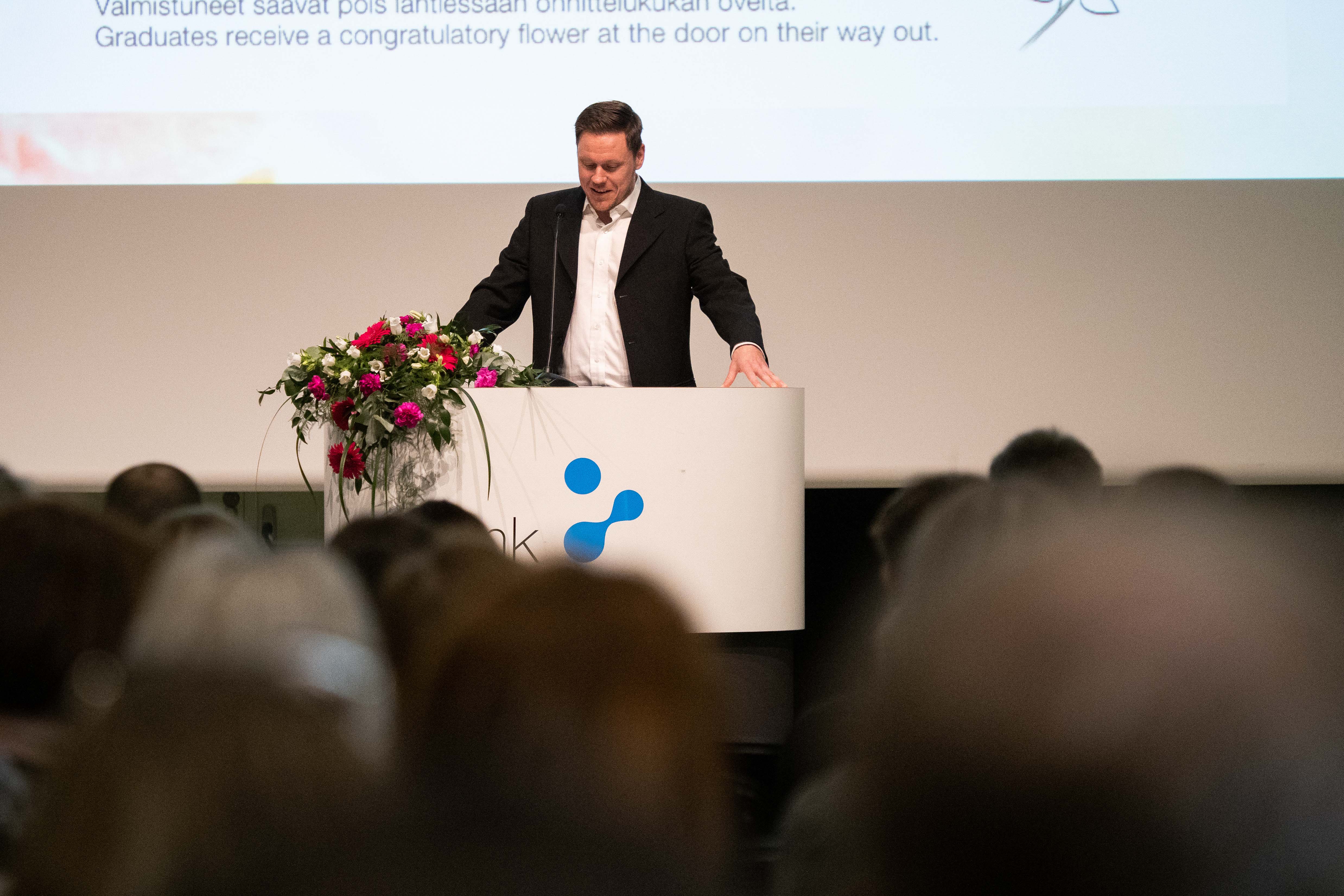 A male person speaks to the audience from a lectern.