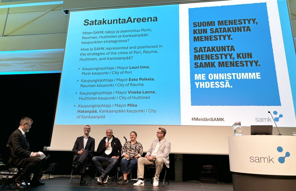 Haastattelija ja neljä haastateltavaa istuvat lavalla.