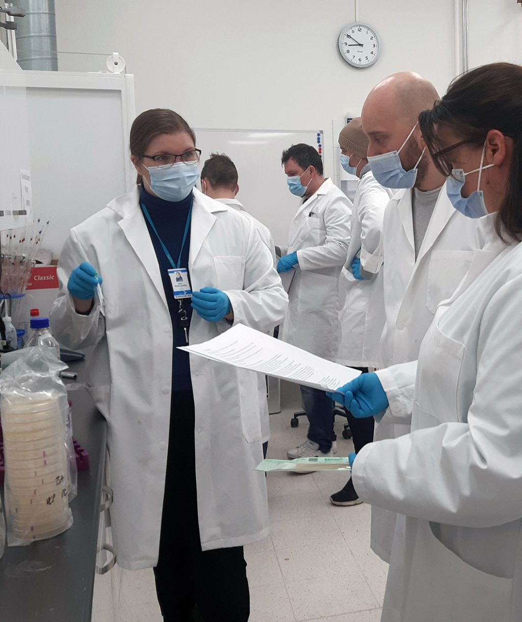 Henkilöitä laboratoriossa takit päällä ja kasvomaskit naamalla.