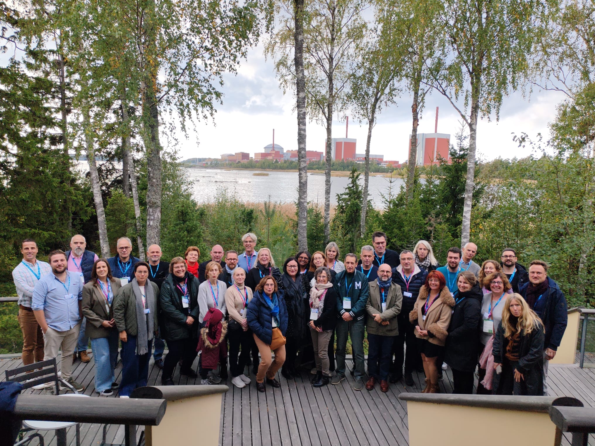 Group photo of conference participants, with the Olkiluoto nuclear power plant in the background.