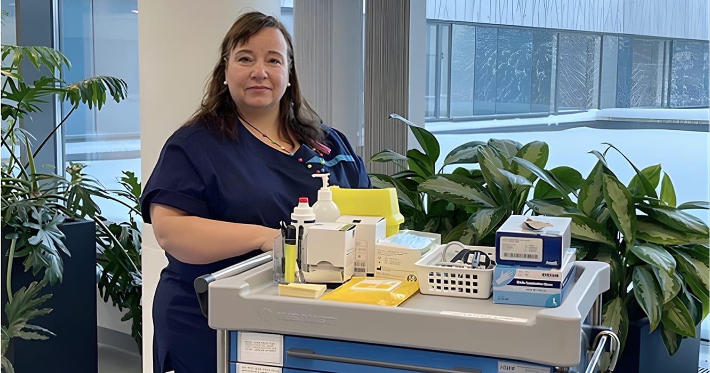 Aune Isosomppi seisoo hoitajan asussa haavakiertokärryn vieressä.