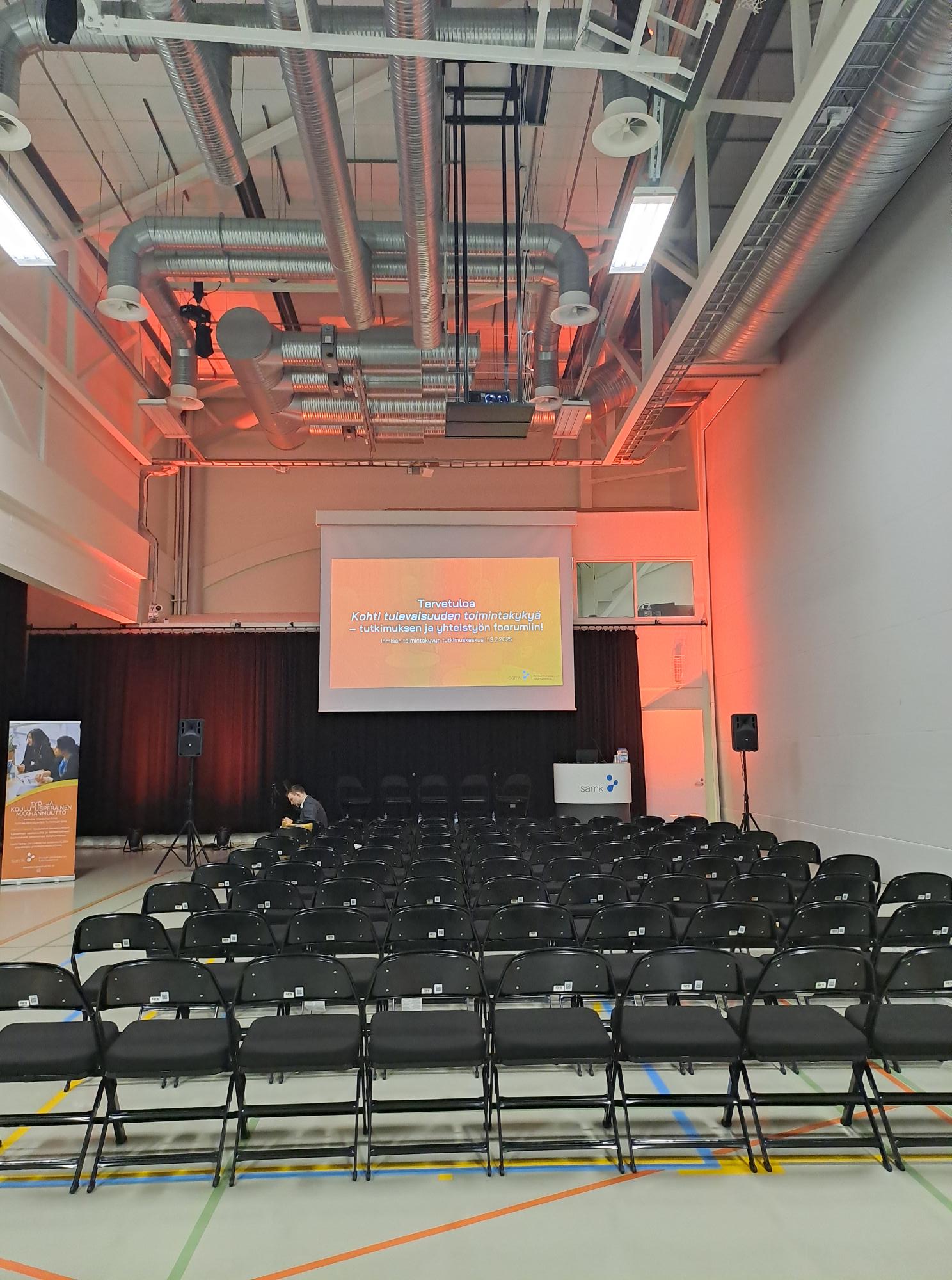 Tuolirivit valkokankaan edessä liikuntasalissa.