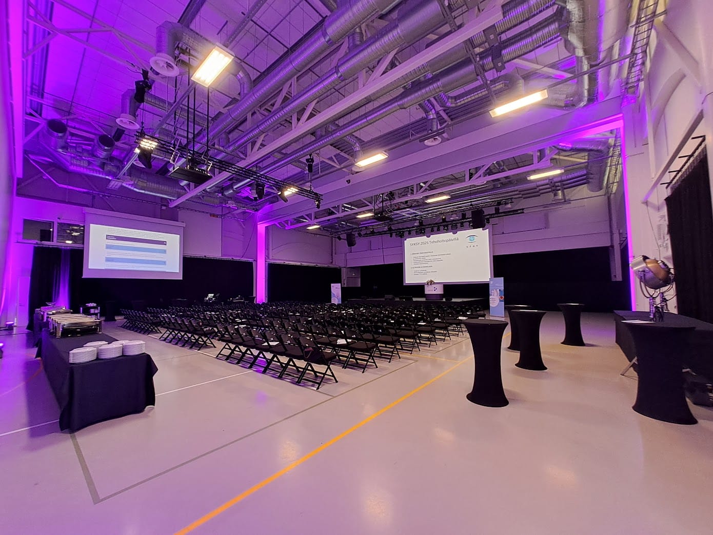 Tuolirivit valkokankaan edessä juhlavalaistussa liikuntasalissa.