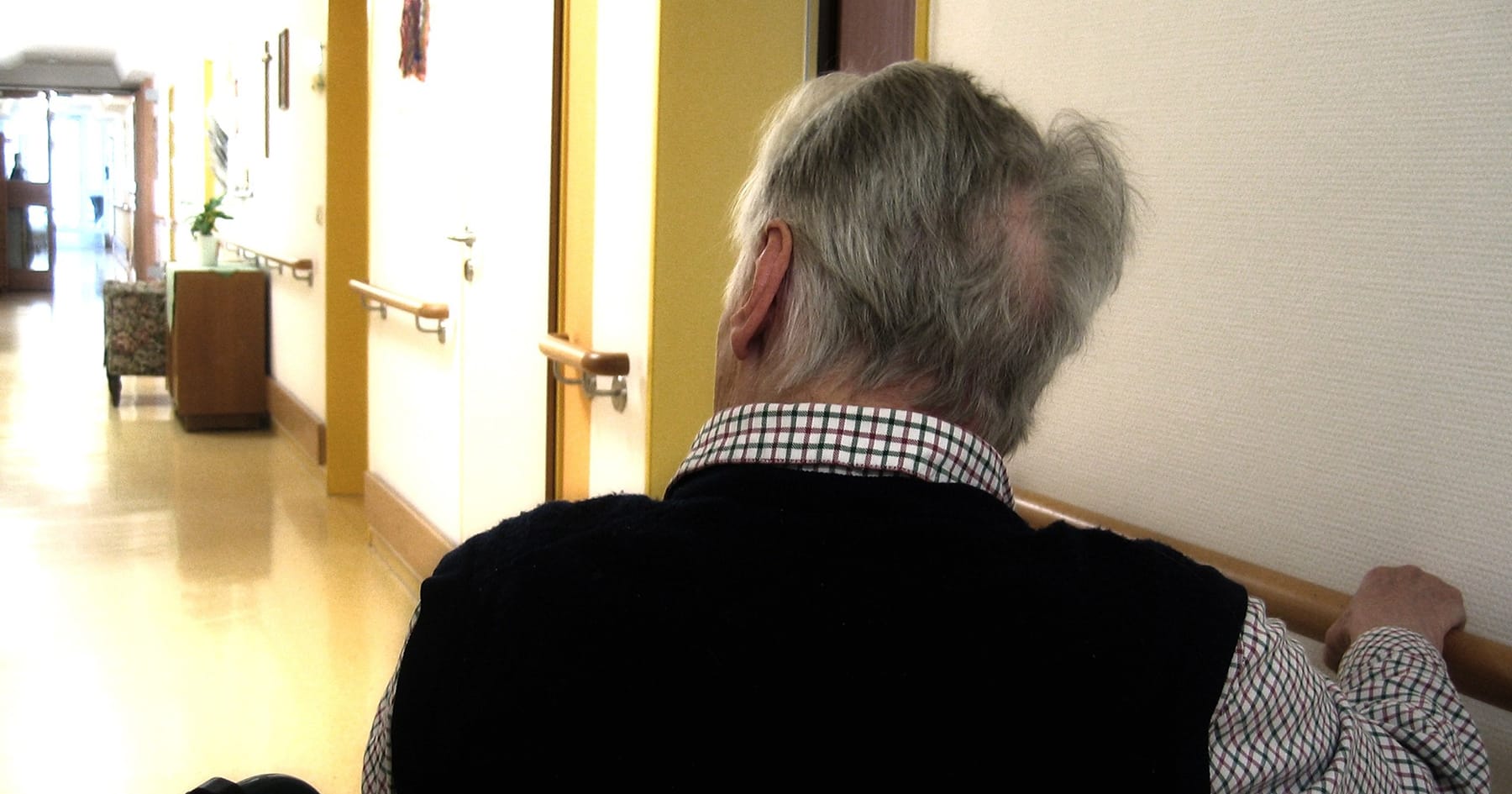 Vanha mies on käytävällä selin kameraan.