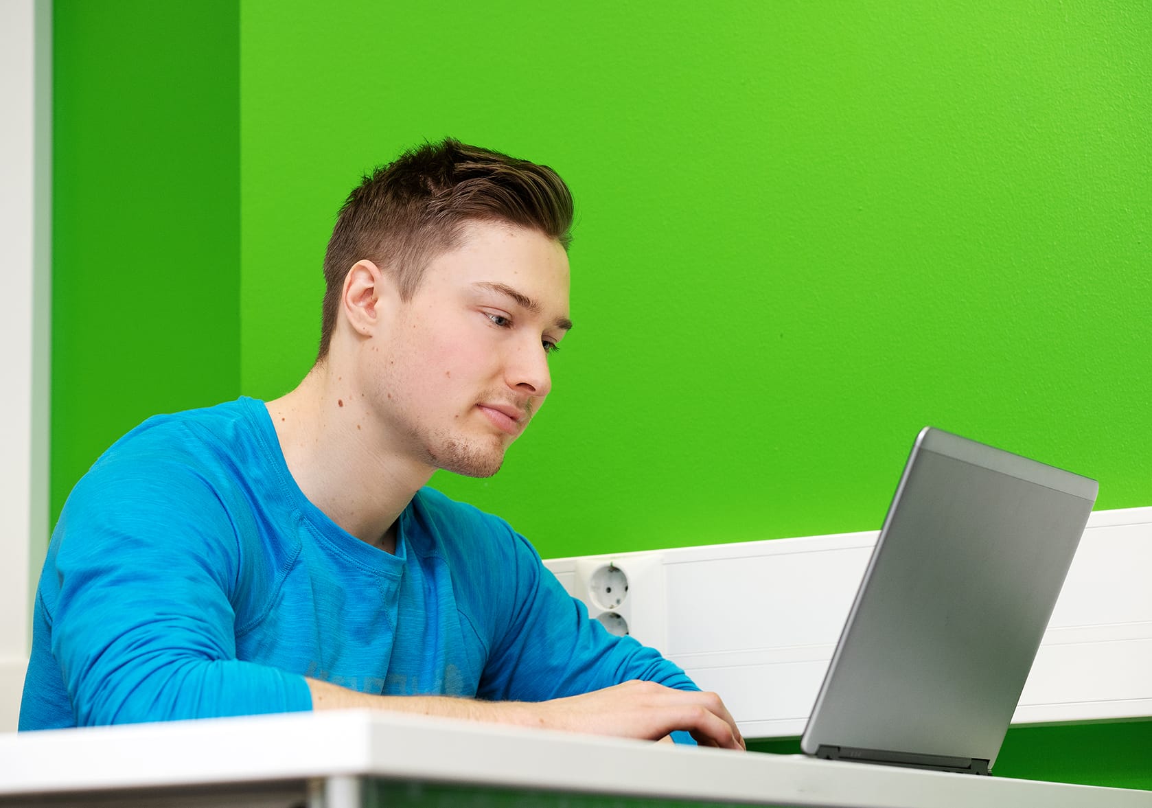 Sinipaitainen opiskelija näpyttelee kannettavaa tietokonetta.