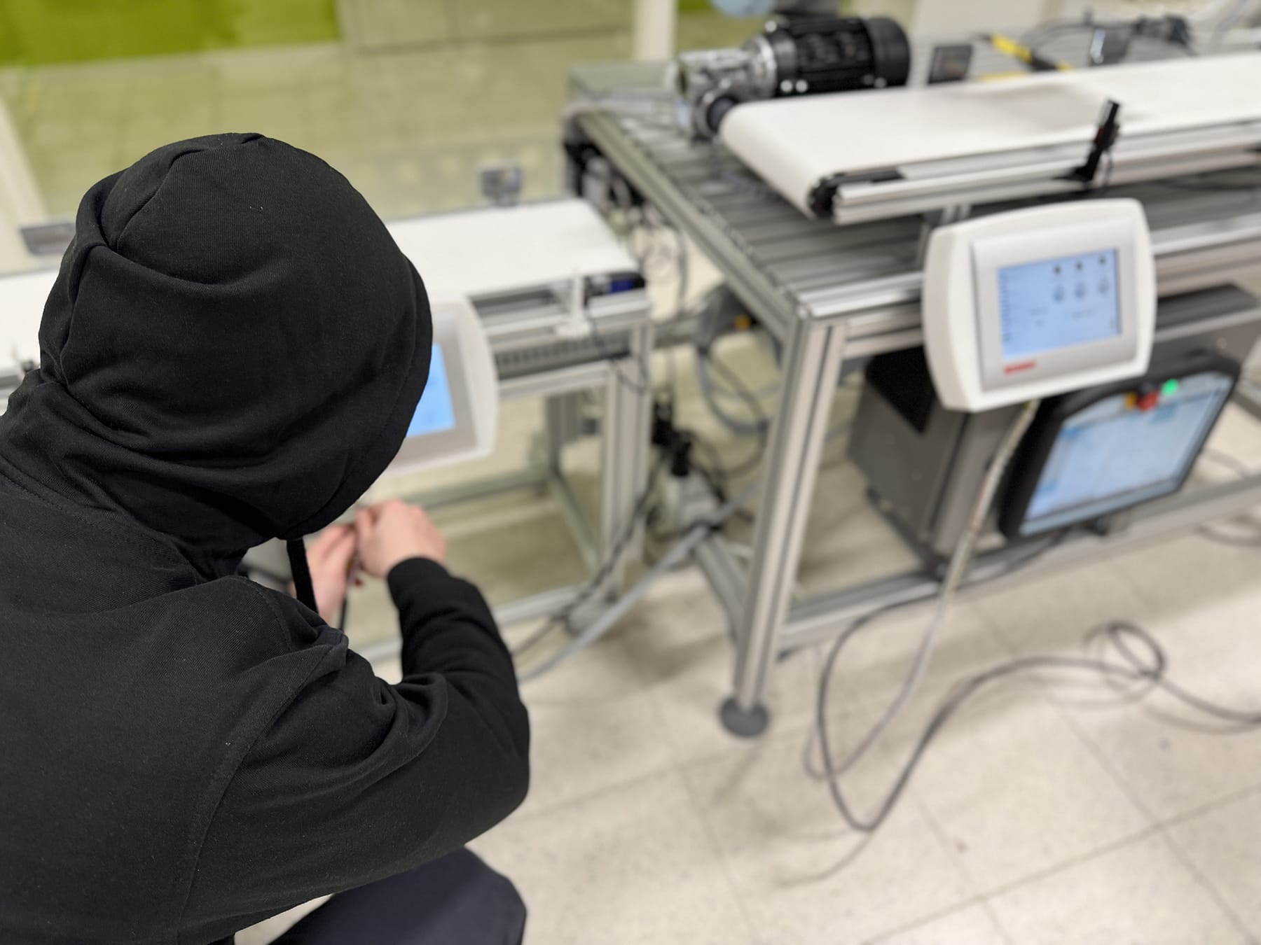 A person wearing a hoodie is working with technical equipment assembly and touchscreens.